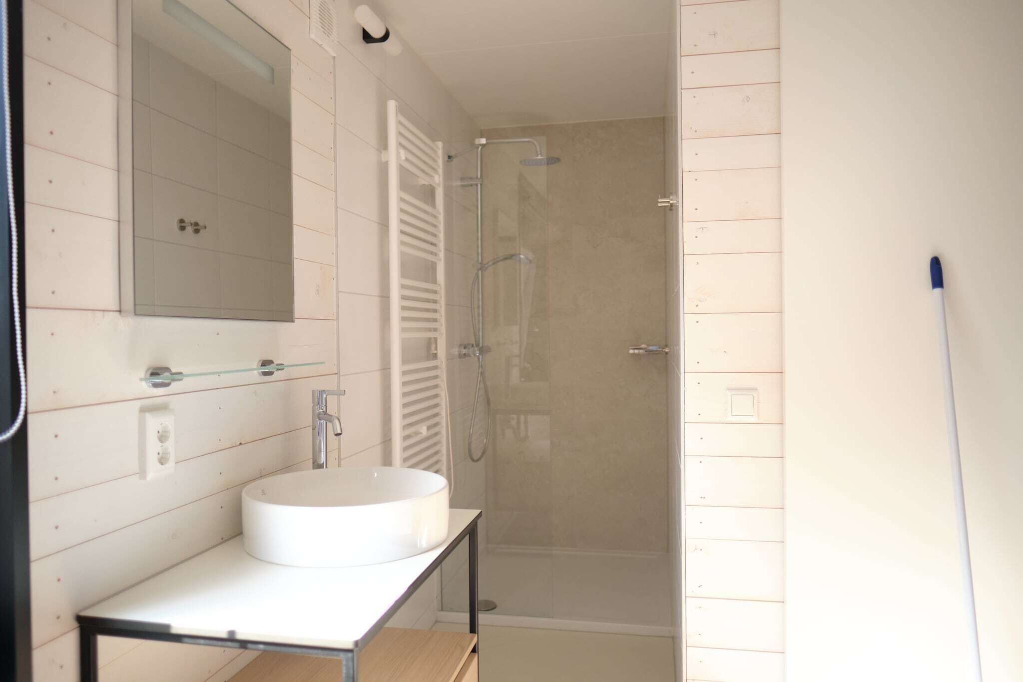 Un baño moderno con un lavabo redondo, un espejo grande y una ducha con cerramiento de vidrio.