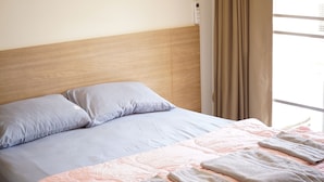 A neatly made bed with a headboard, a window with curtains, and an air conditioning unit on the wall. - The Parkland Bangna Next MRT Station (Bangkok)