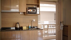 A compact kitchen with wooden cabinets, a built-in microwave, a coffee maker, and a sink. - The Parkland Bangna Next MRT Station (Bangkok)