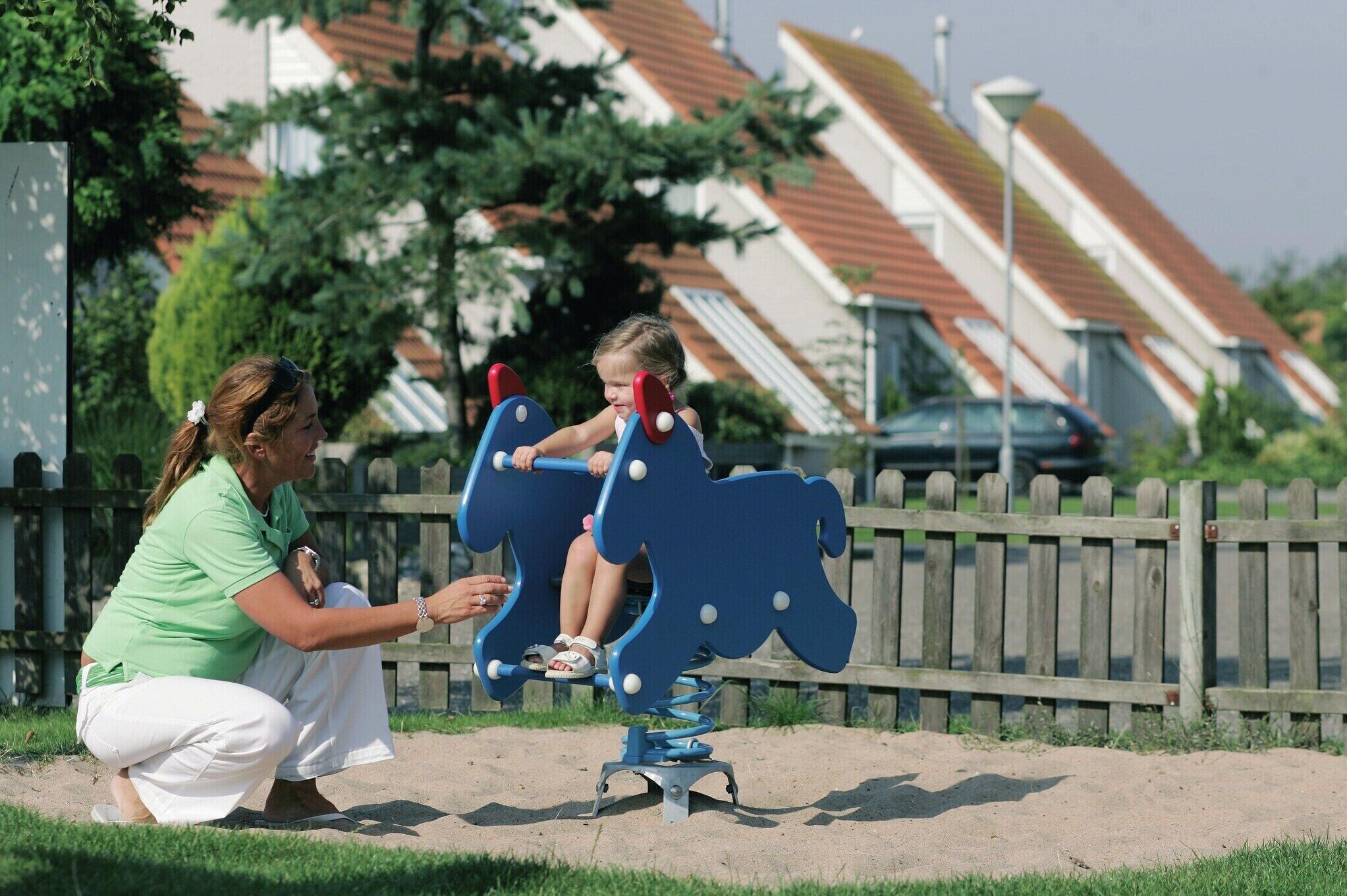 Een speeltuin met een schommelset in de vorm van een blauw paard.