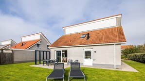 Et toetagers hus med røde tegltagsten, en terrasse med to liggestole og en lille have.