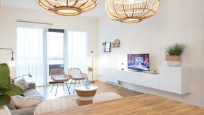 Un salon moderne avec des meubles en osier, une table à manger en bois et un téléviseur posé sur un meuble blanc.
