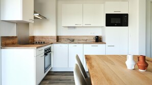 A modern kitchen with white cabinets, a wooden countertop, a built-in oven, a microwave, and a dining table with chairs. - Comfortable Villa in Berck (Berck-Sur-Mer)