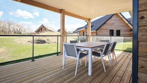 A covered outdoor area with a wooden deck, a table with chairs, and a view of a house in the background. - Comfortable Villa in Berck (Berck-Sur-Mer)