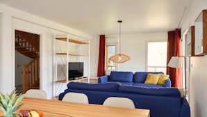 A modern living room with a blue sofa, wooden dining table, and a television. - Beach House in France near the Coast (Berck-Sur-Mer)