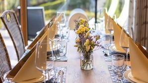 Une table à manger avec des chaises, un vase rempli de fleurs et de beaux verres transparents.