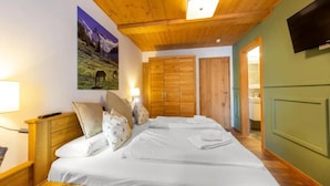 Une chambre d’hôtel avec un grand lit, une tête de lit en bois, un téléviseur fixé au mur et un tableau représentant un paysage de montagne.