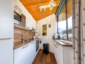 Eine kleine Küche mit weißen Schränken, einer Holz Arbeitsplatte, einem Einbauofen und einem Fenster mit Vorhängen.
