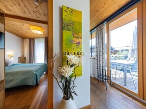A hotel room with a bed, a painting, a vase with flowers, and a view of the outdoors.