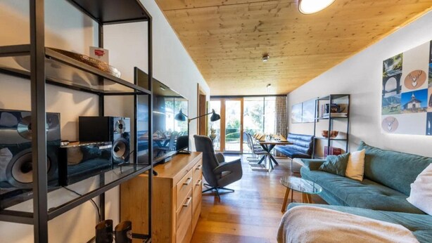 Un salon moderne avec un plafond en bois, un canapé, une table basse et une bibliothèque contenant divers objets.