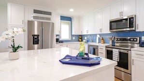 A modern kitchen with stainless steel appliances, white cabinetry, and a marble countertop.