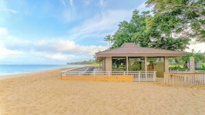 A beachside gazebo with a roof and glass walls, overlooking the ocean.