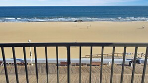 A beach view from a balcony with a wooden deck, a sandy beach, and the ocean.