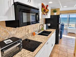 A kitchen with a microwave, stove, and sink, with a view of the beach through the window. - Direct Oceanfront and Boardwalk Condo on 12th St. with Indoor Pool! Decatur House 505 (Ocean City)
