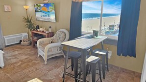 A dining area with a view of the beach, a wicker chair, a table, and a hanging lamp.