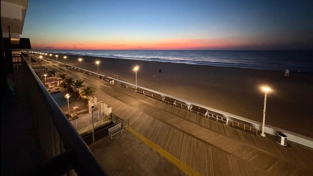 A beach view with a wooden boardwalk, street lamps, and a railing along the water's edge.