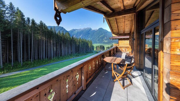 A wooden deck with a table and chairs, overlooking a forest and mountains.