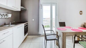 A modern kitchen with white cabinets, a stove, and a dining area with a table and chairs. - Apartment on Pag Island near Seabeach (Novalja)