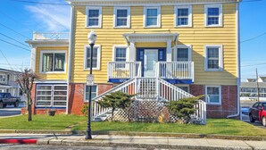 A yellow two-story house with a front porch, a small front yard, and a street view.