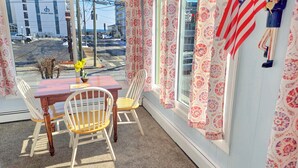 A room with a table and chairs, a window with floral curtains, and an American flag.