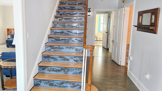 A staircase with blue painted steps and a wooden handrail, leading to a landing with a door.