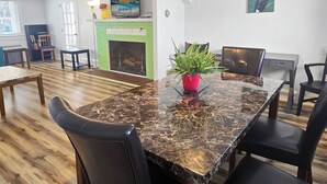 Un coin repas avec une table en marbre, des chaises noires, une plante en pot, un téléviseur et une cheminée.
