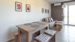 Una sala de estar moderna con una mesa de comedor de madera, bancos y un sofá con cojines. Hay tres cuadros en la pared.