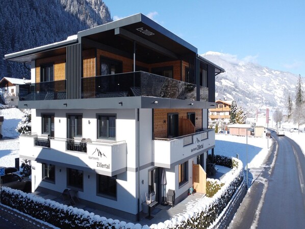 Ein modernes mehrgeschossiges Gebäude mit Balkon, mit der Aufschrift "Apartments Zillertal", in einer verschneiten Berglandschaft.