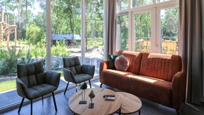 A modern living room with a large window, two armchairs, a sofa, and a coffee table. - Stylish Hoenderloo Family Bungalow (Hoenderloo)