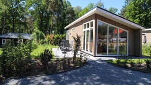 A modern house with a large glass window, surrounded by a garden and trees. - Stylish Hoenderloo Family Bungalow (Hoenderloo)