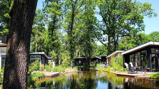 A tranquil outdoor setting with a pond, modern buildings, and lush greenery. - Stylish Hoenderloo Family Bungalow (Hoenderloo)