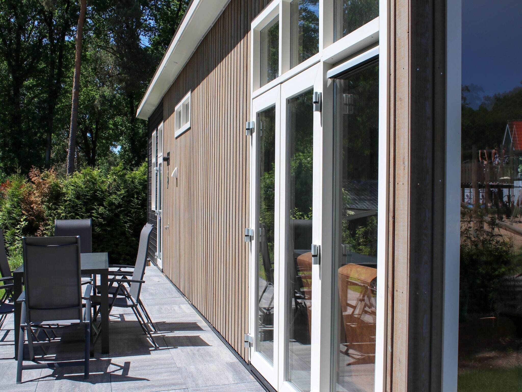 A modern building with large glass doors, a patio with outdoor furniture, and a view of a playground.