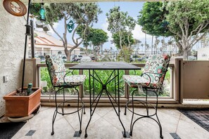 Een terras buiten met een tafel en twee stoelen, een hangende vogelvoeder en uitzicht op de straat en bomen.