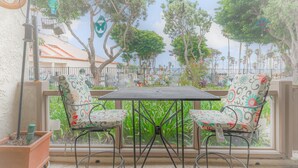 Un balcon avec deux chaises et une table, donnant sur un jardin agrémenté d’arbres et de fleurs.