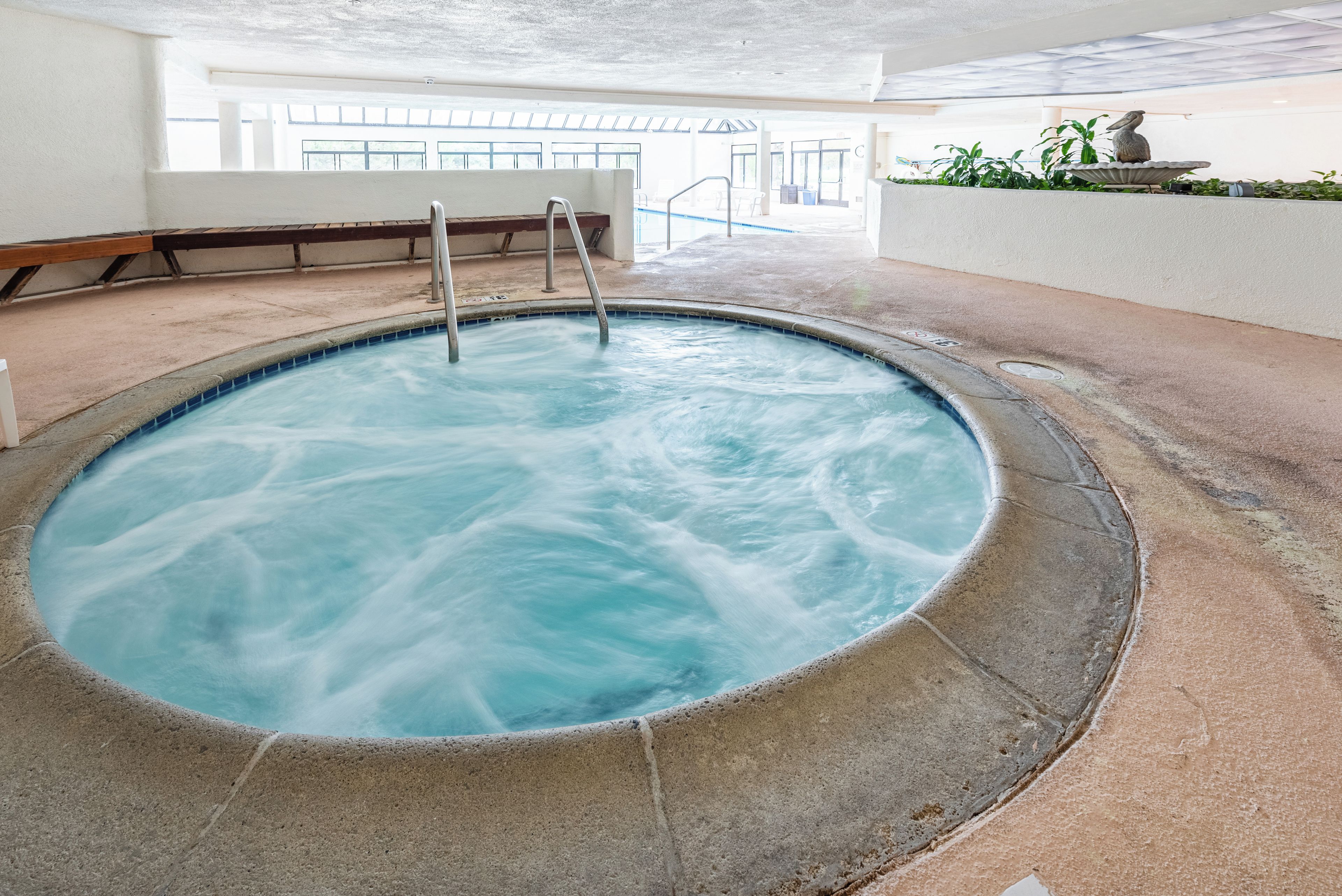 Une piscine intérieure dotée d’un bord en béton, d’une terrasse en bois et d’un banc.