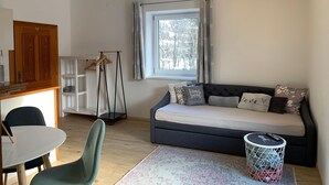 Een knusse woonkamer met een bank, een eettafel en een raam met gordijnen.