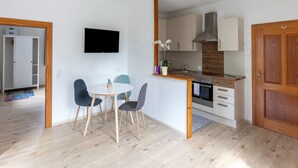Een moderne keuken met een inbouwoven, een eethoek met een ronde tafel en stoelen, en een aan de muur bevestigde televisie.