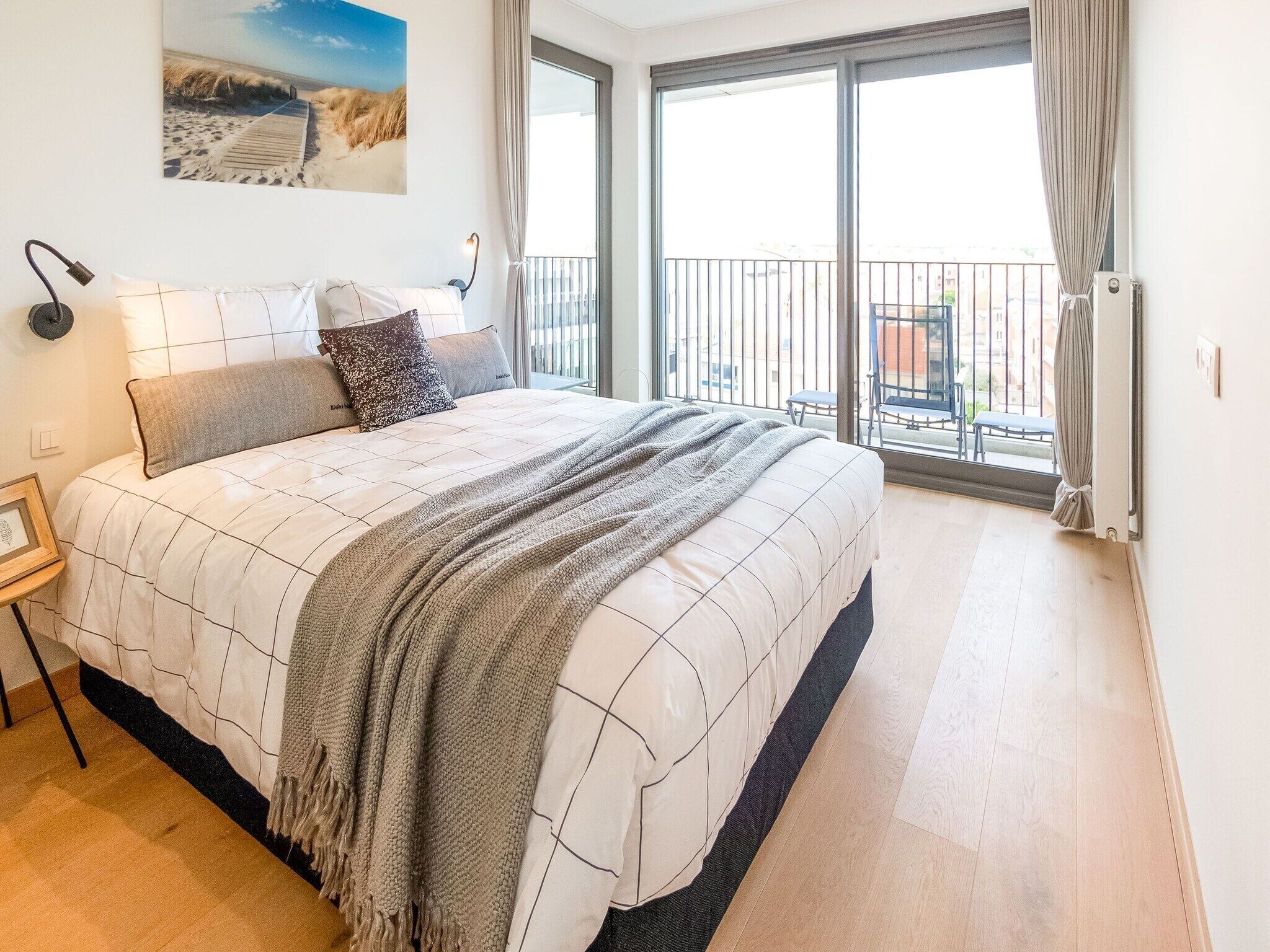 Un dormitorio con cama, mesita de noche, lámpara, un cuadro en la pared y balcón con vistas.