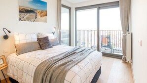 Een slaapkamer met een bed, nachtkastje, lamp, foto aan de muur, en een balkon met uitzicht.