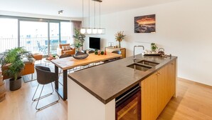 Een moderne keuken met een centraal eiland, een zithoek met een bank en stoelen, en een groot raam met uitzicht op de stad.