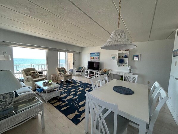 A spacious living area with a view of the sea, white furniture, and a dining table.