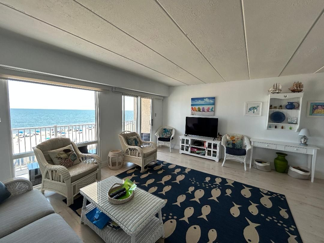 A living room with a view of the sea, furnished with wicker chairs and a sofa, a flat-screen TV, and a coffee table.