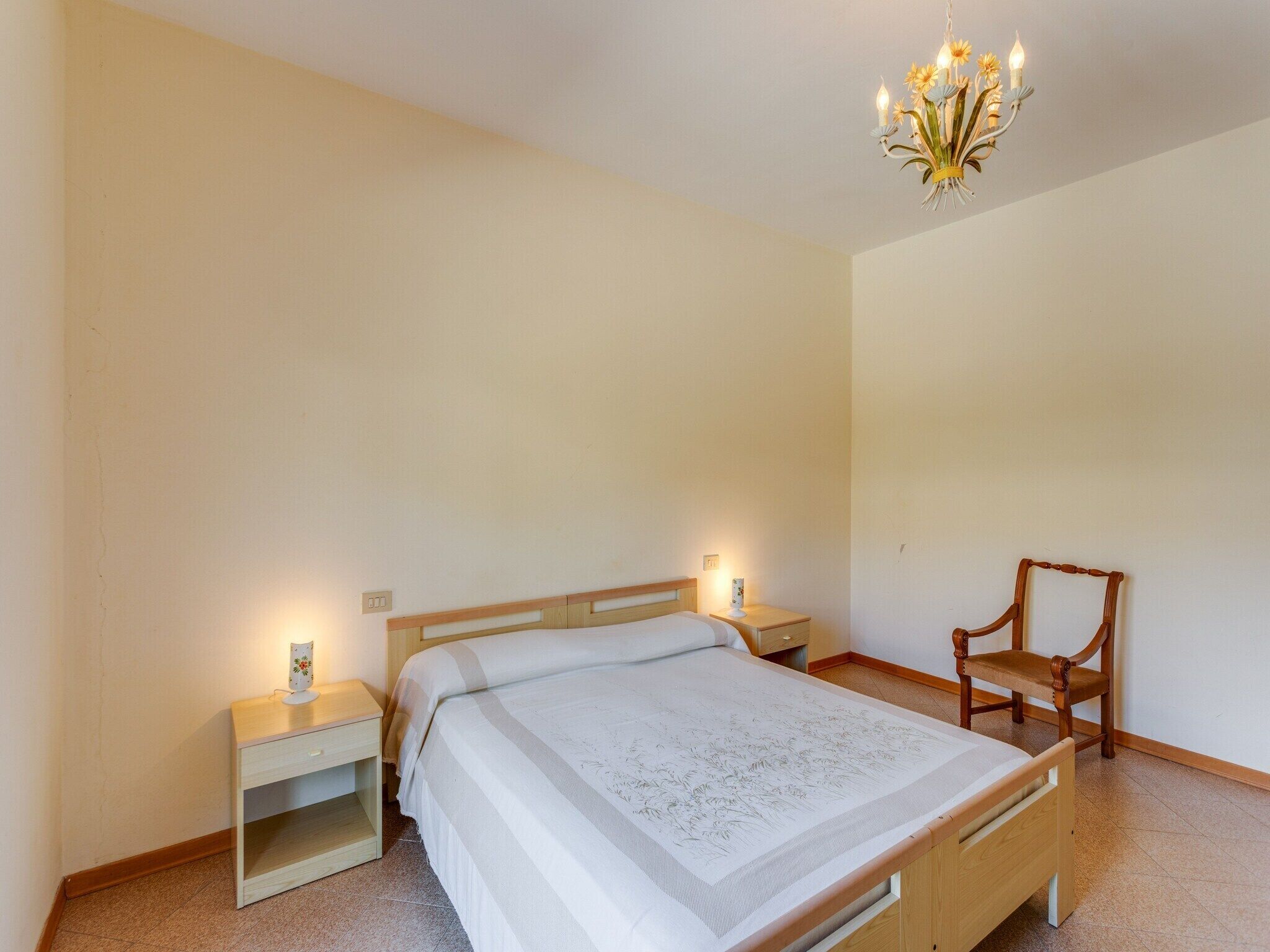 Una camera da letto con un letto, due comodini, una sedia e un lampadario.