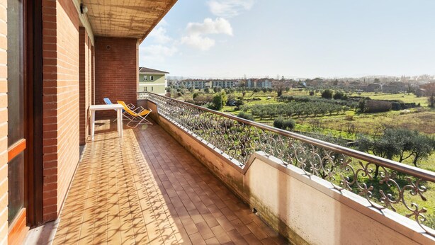 Un balcón con vista a una zona residencial, un muro de ladrillo y una barandilla metálica.