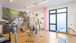 Un gimnasio con equipo cardiovascular, máquinas de pesas y un mural de un bosque.