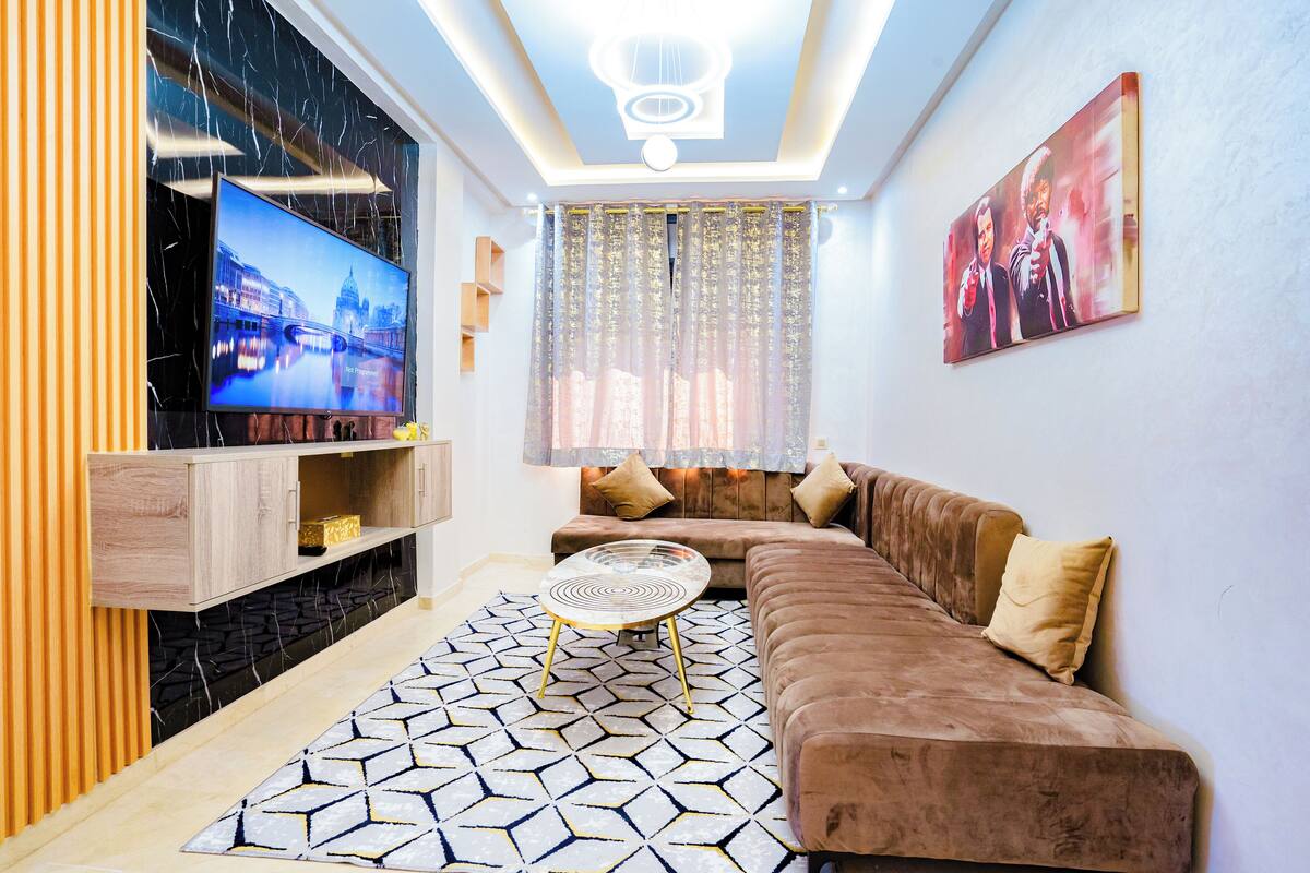 Uma sala de estar moderna com um sofá seccional, uma TV de tela plana, um tapete decorativo e um lustre.
