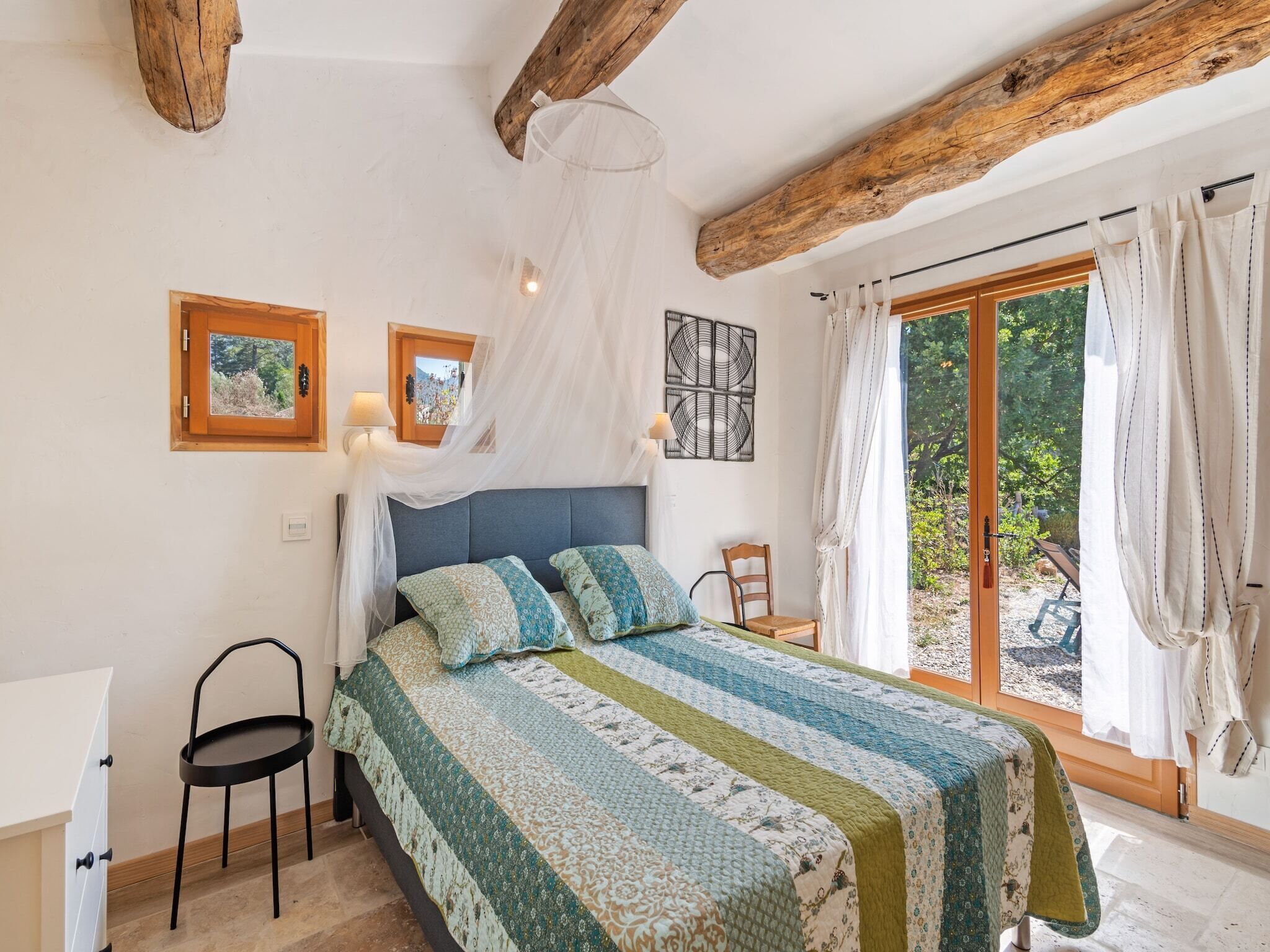 Een slaapkamer met een bed, een stoel, een bureau en een groot raam.