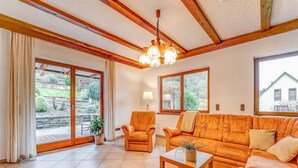 A living room with a sofa set, a coffee table, and a chandelier. There are large windows and a view of the outside. - Spacious flat in Adenau near the Nürburgring (Adenau)