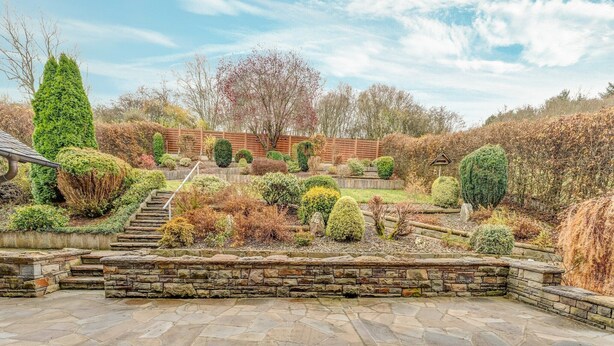 A stone patio with a wooden deck, surrounded by a landscaped garden with various shrubs and a wooden fence in the background. - Spacious flat in Adenau near the Nürburgring (Adenau)