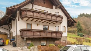 A two-story chalet with a balcony, stone facade, and a car parked in front. - Spacious flat in Adenau near the Nürburgring (Adenau)